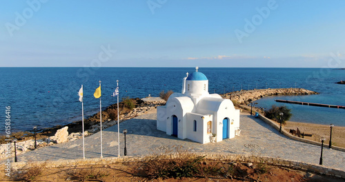 Drone shooting a small beautiful white church or Chapel of St. Nicholas with a blue dome and a door on the shore of a calm deep sea in Protaras Cyprus. photo