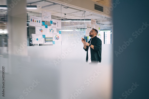 Male entrepreneur drawing on glass wall working with charts
