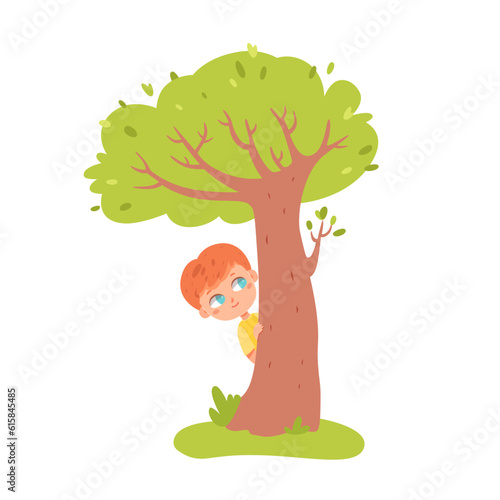 Cute boy playing hide and seek, peeping over green tree, small kid hiding in summer park