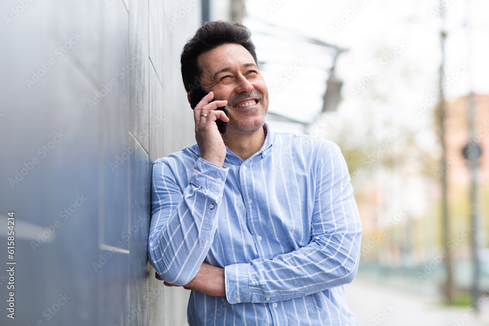 Smiling mature man leaning against wall and talking on cellphone Smiling mature man leaning against wall and talking on cellphone