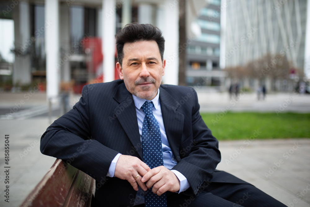 Mature latin businessman sitting on bench outside in the city Mature latin businessman sitting on bench outside in the city