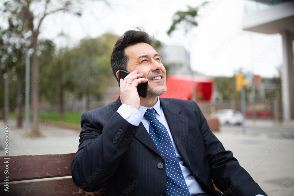 Happy mature businessman sitting on bench talking on mobile phone Happy mature businessman sitting on bench talking on mobile phone