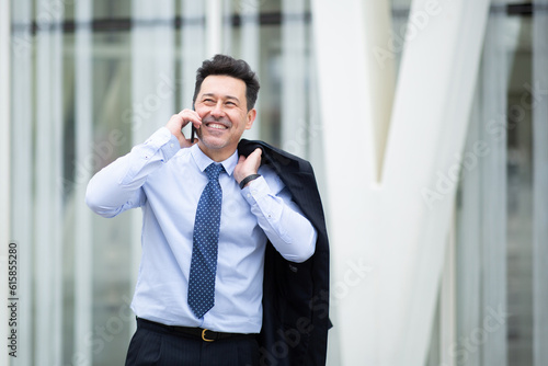 Smiling older businessman walking outside talking on mobile phone