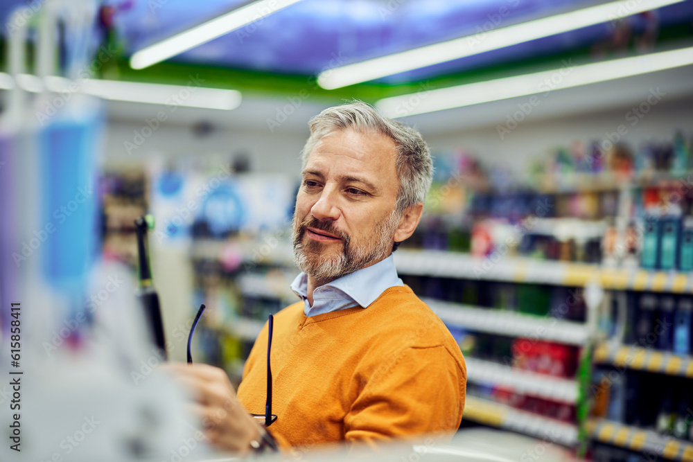 A smiling male customer holding an electric toothbrush in a supermarket. A smiling male customer holding an electric toothbrush in a supermarket.
