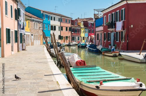 Colorful houses along the canal with parked boats on Burano island, Venice, Italy. Attractive famous travel destination.