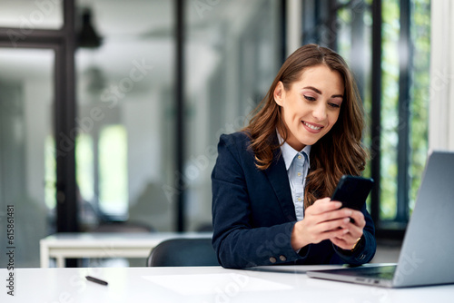 A smiling businesswoman using a mobile phone while sitting in front of a laptop.