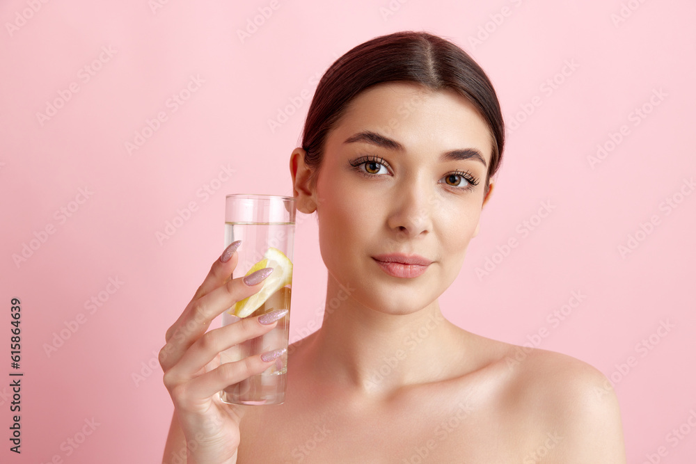 Beautiful young woman with healthy, well-kept skin taking care after health, drinking water with lemons against pink studio background. Concept of natural female beauty, body and skincare, health, ad Beautiful young woman with healthy, well-kept skin taking care after health, drinking water with lemons against pink studio background. Concept of natural female beauty, body and skincare, health, ad