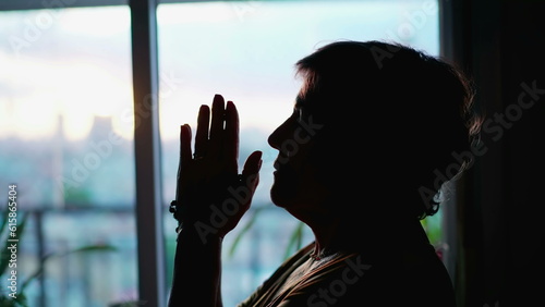 Silhouette of a senior woman in Prayer at hoem suring sunset. Contemplative meditative elderly person praying to God photo