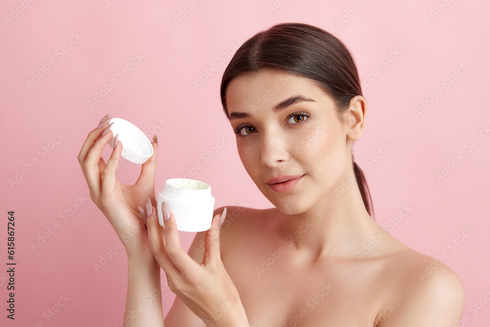 Portrait of young beautiful woman posing with face moisturizing cream against pink studio background. Skin hydration. Concept of natural female beauty, body and skincare, cosmetology, health, ad Portrait of young beautiful woman posing with face moisturizing cream against pink studio background. Skin hydration. Concept of natural female beauty, body and skincare, cosmetology, health, ad