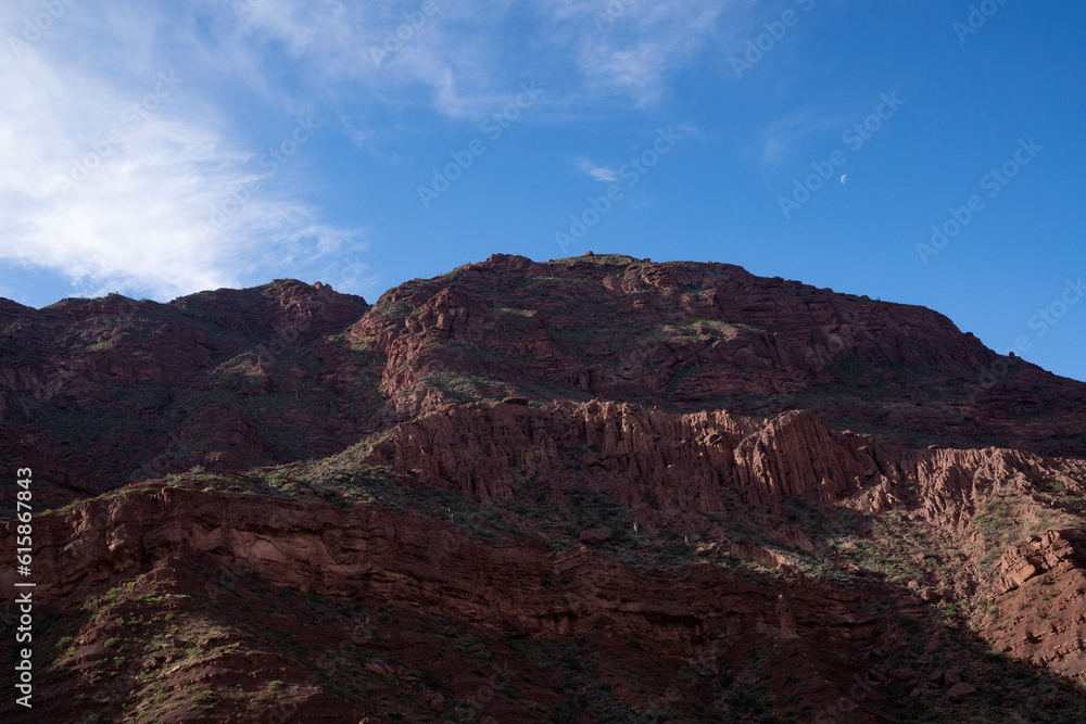 Panorama view of the brown rocky mountain peak and cliffs in the desert, under a blue sky.