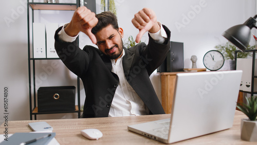 Dislike. Upset indian businessman guy working on laptop computer at home office thumbs down sign gesture, expressing discontent, disapproval, dissatisfied bad work. Displeased serious freelancer man photo