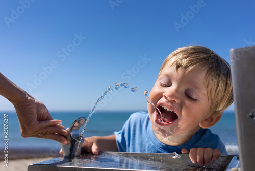 Cuadro en lienzo blond boy 3 years old drinks water from a water fountain on the beach in summer