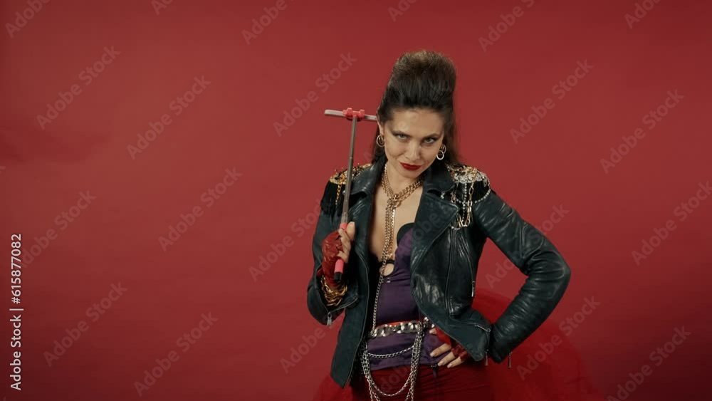 An informal woman takes a selfie on a smartphone using a monopod. Woman with bright makeup, fleece and in a leather jacket with chains in the studio on a red background. Advertising. An informal woman takes a selfie on a smartphone using a monopod. Woman with bright makeup, fleece and in a leather jacket with chains in the studio on a red background. Advertising.