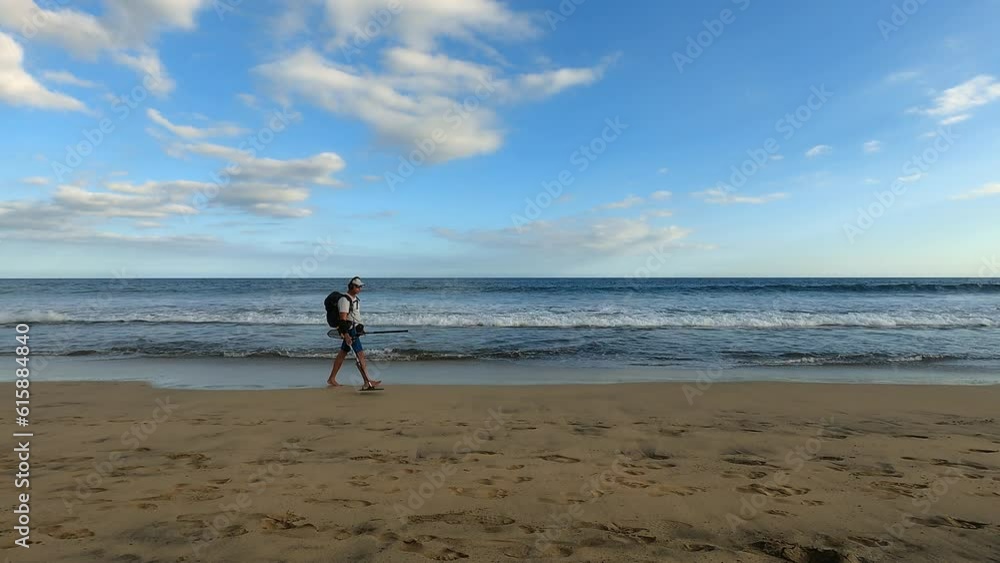 Man with metal detector searching for precious objects and coins at beach and sea enjoying colorful sunset with cloudy sky Man with metal detector searching for precious objects and coins at beach and sea enjoying colorful sunset with cloudy sky
