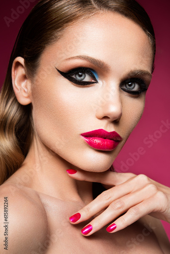 Beautiful young female face with bright fashion multicolored make-up on a pink background