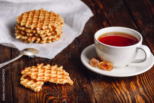 White Cup of Tea with Waffles Stack on Napkin and Pieces of Waffle on Wooden Surface.