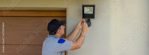 Image of an electrician on a scissor ladder using his tools to install a spotlight on a house. Illumination of the darkest parts of the house. Horizontal banner 

