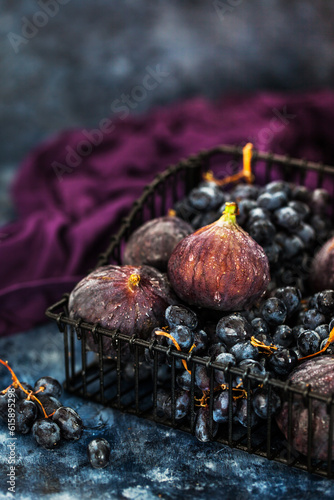 Fresh figs and purple grape in basket on dark wooden background