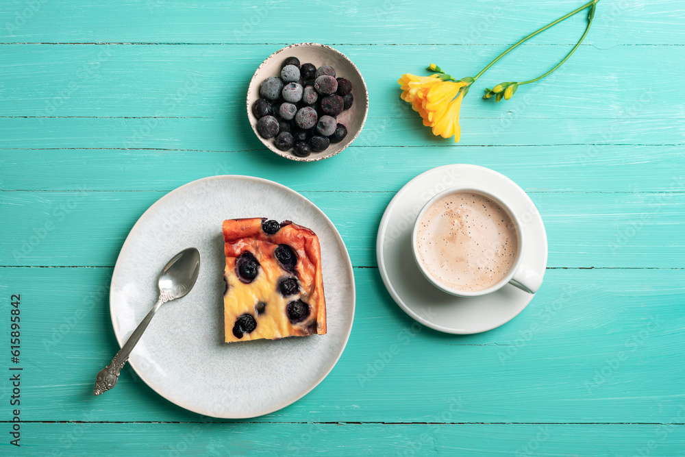 A cup of coffee and blueberry cake, frozen blueberries and yellow freesia flower on turquoise wooden table. Top view, flat lay A cup of coffee and blueberry cake, frozen blueberries and yellow freesia flower on turquoise wooden table. Top view, flat lay