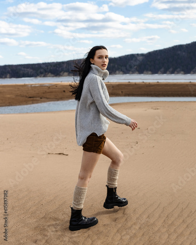 Caucasian young pretty stylish woman near river lake water street on sand pier dressed brown trench coat hold handbag smiling poses outside city, spring autumn