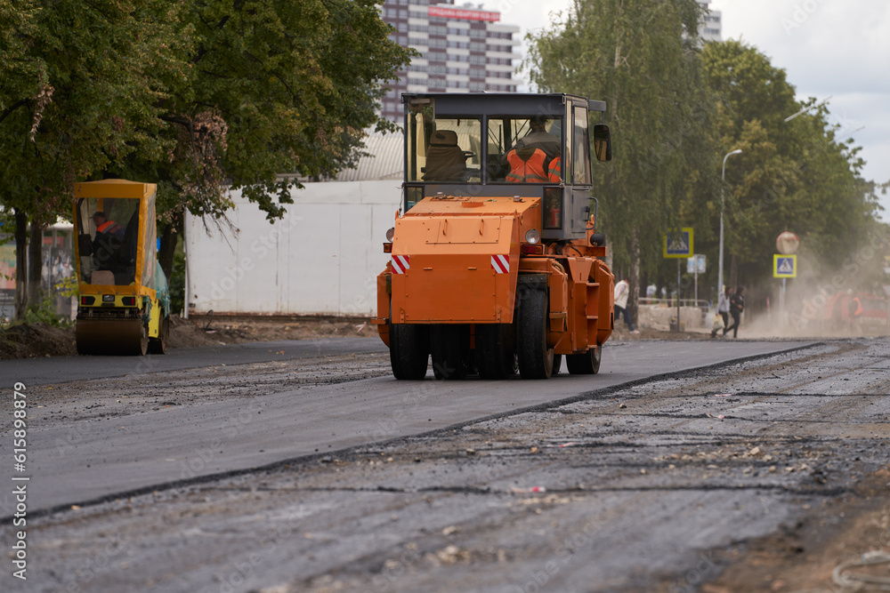 A pneumatic-wheeled road roller levels and compacts the asphalt roadway under repair in the city.
