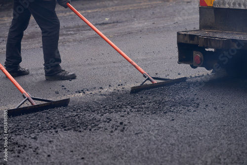 Construction of the highway. Laying of asphalt mortar. Fragment of the asphalt paver and road workers with hand tools leveling the edge of the roadway.