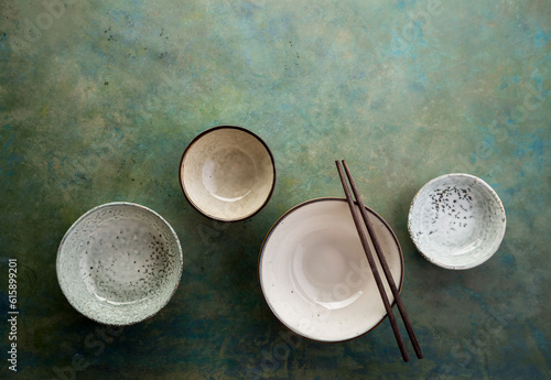 Empty ceramic bowls and chopsticks on green background with copy space. Top view.
