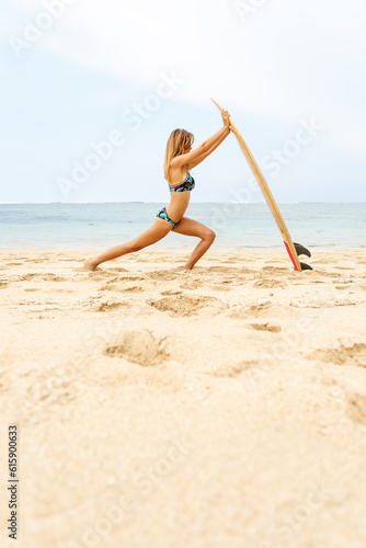 Beautiful happy surfing fit girl in sexy bikini lycra stretching before yoga with wooden surf shortboard surfboard board at sunrise or sunset. Vacation concept. Summer holidays. Tourism, sport.
