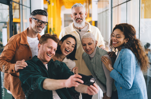 Group of smiling diverse people recording video on smartphone in office