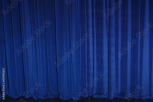 Theatrical curtain is closed, illuminated by spotlights of rich bright blue color.