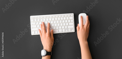 Hands of woman using computer keyboard and mouse on dark background, top view