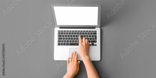 Hands of woman using laptop on grey background, top view