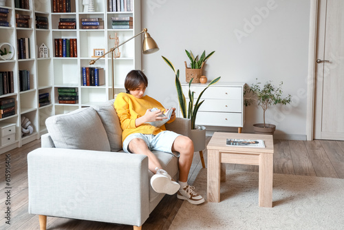 Teenage boy reading book on sofa at home