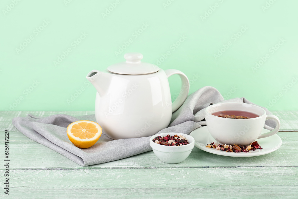 Cup of fruit tea, teapot and lemon on green wooden table Cup of fruit tea, teapot and lemon on green wooden table