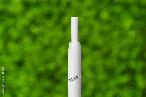 Modern electronic cigar with stick against green nature background