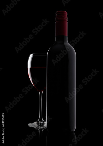 Glass of red wine with bottle with shape on black background with reflection