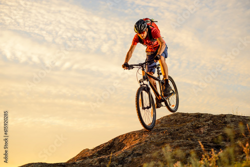 Cyclist in Red T-Shirt Riding the Bike Down the Rock on the Sunset Sky Background. Extreme Sport and Enduro Biking Concept.
