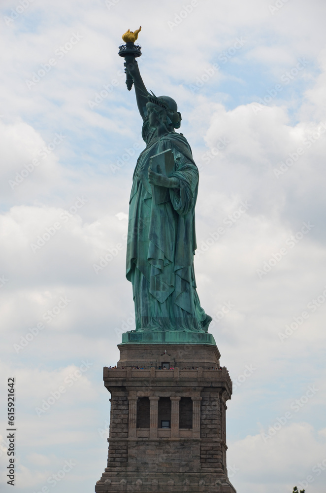 Fototapeta premium The Statue of Liberty on Liberty Island under cloudy sunny skies