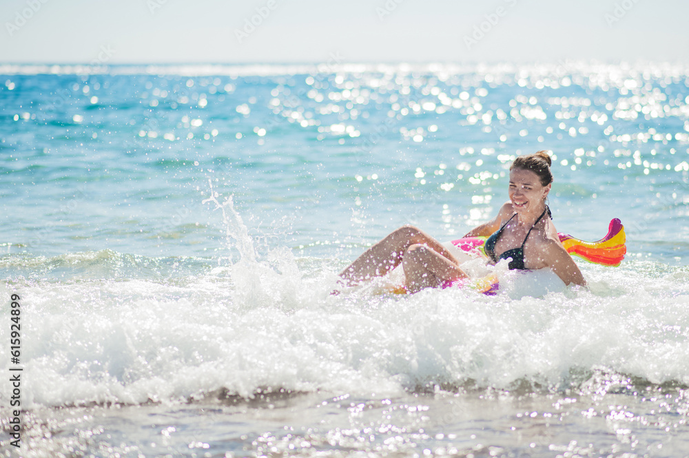 Happy young woman on inflatable unicorn ring bathes in waves. Summer vacation at sea..