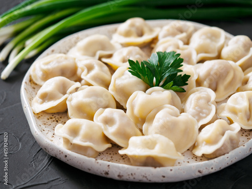 Traditional russian pelmeni, ravioli, dumplings with meat on black concrete background. Russian food and russian kitchen concept.