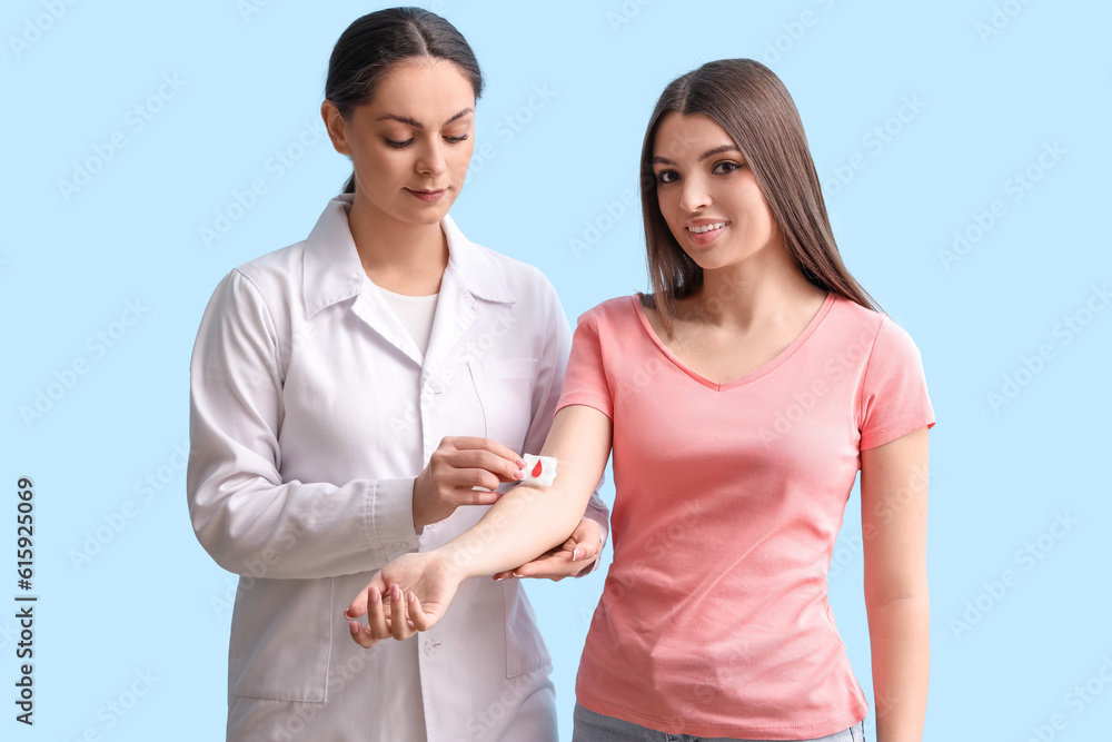 Female doctor applying gauze on blood donor's arm against blue background