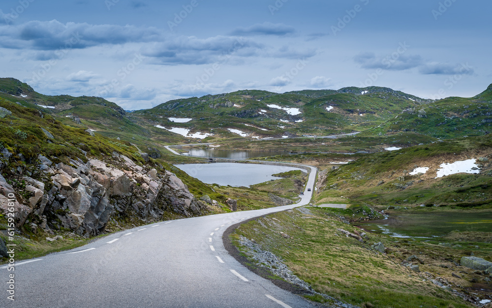 Scenic mountain road through the rocks and lakes with some snow on the green hills. Norway summer. Scenic mountain road through the rocks and lakes with some snow on the green hills. Norway summer.