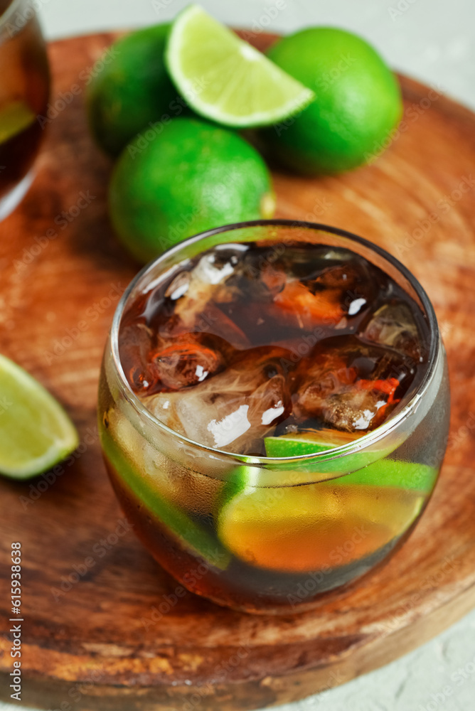 Board with glass of cold Cuba Libre cocktail and limes on grey background Board with glass of cold Cuba Libre cocktail and limes on grey background