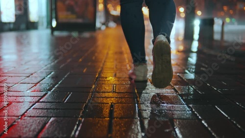 Rear view of the legs of a girl walking in front of the camera on a wet road