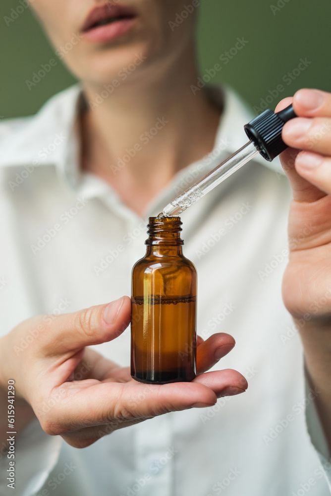 essential oil in a brown bottle with a pipette in the hands of a woman on a green background. Women's hands with a bottle of oil and a pipette - the sphere of beauty