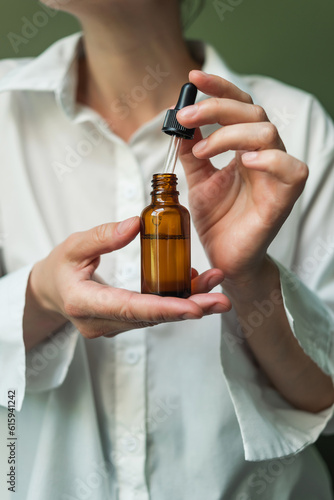 Obraz na płótnie Essential oil with a pipette in the hands of a woman on a green background. Women's hands with a bottle of oil and a pipette - the sphere of beauty w salonie