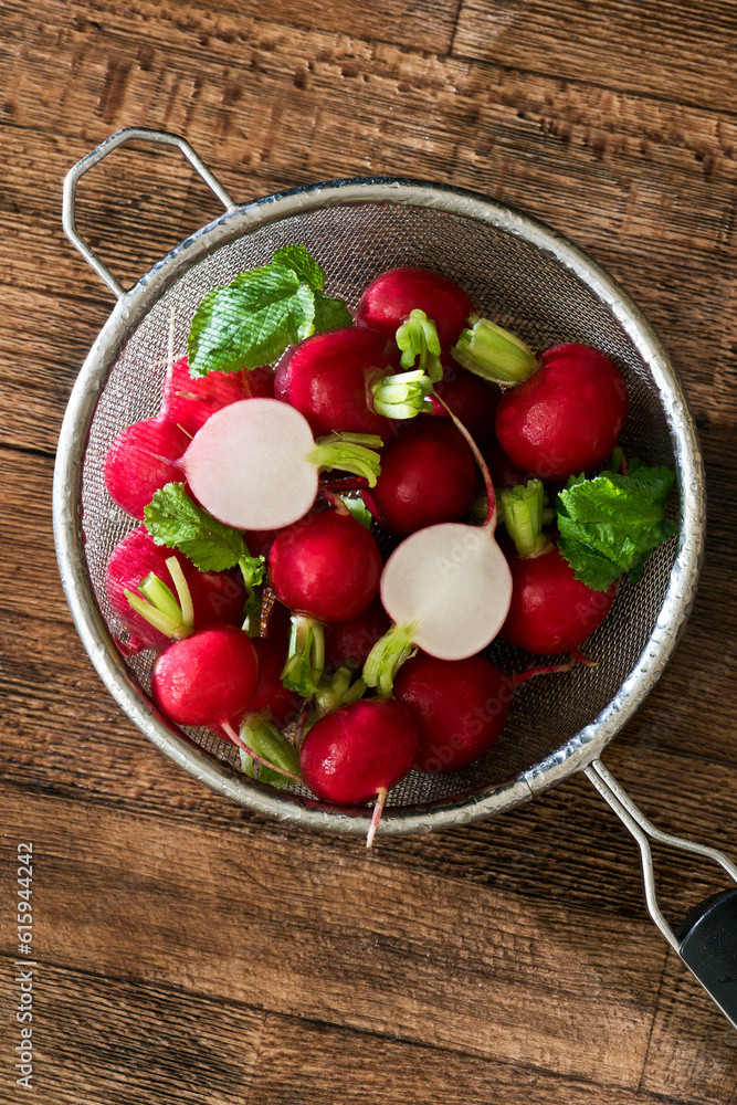 Several washed red radishes in a sieve on a wooden board Several washed red radishes in a sieve on a wooden board
