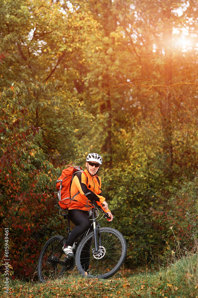 Fototapeta premium Candid outdoor shot of concentrated young rider in protective gear and track suit sitting on his bike in the depth of the forest. He is stuck to healthy lifestyle.