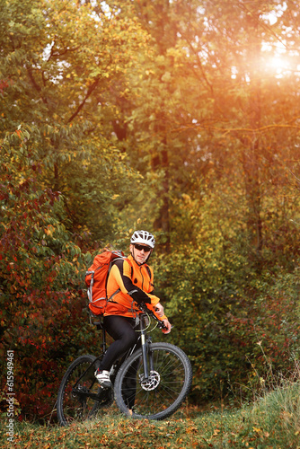 Fototapeta Naklejka Na Ścianę i Meble -  Candid outdoor shot of concentrated young rider in protective gear and track suit sitting on his bike in the depth of the forest. He is stuck to healthy lifestyle.