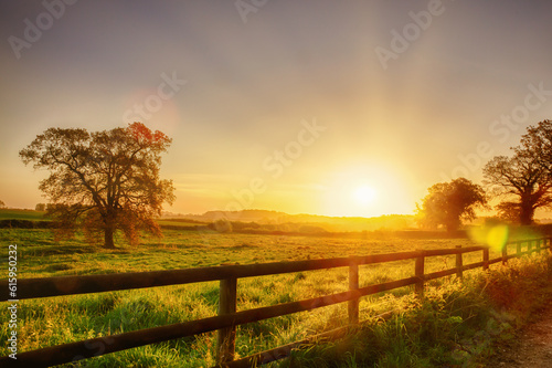 Glorious sunrise over grassy rural landscape in Norfolk UK with a two bar fence disappearing off into the distance.